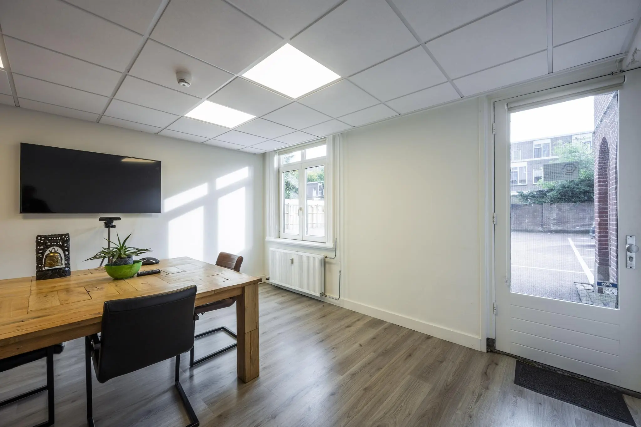 Vergaderruimte aan de Nieuwe Gracht met houten tafel, stoelen, flatscreen-tv en zicht op de buitendeur en parkeerplaats.